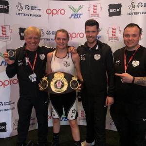 Louise Orton posing for a photo with her amateur boxing team. Louise is holding her England Boxing National Elite Championship belt.